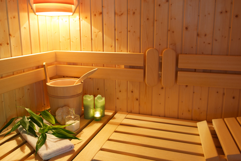 Cozy sauna with green candles, a white towel, bambbo decoration and  other sauna equipment.